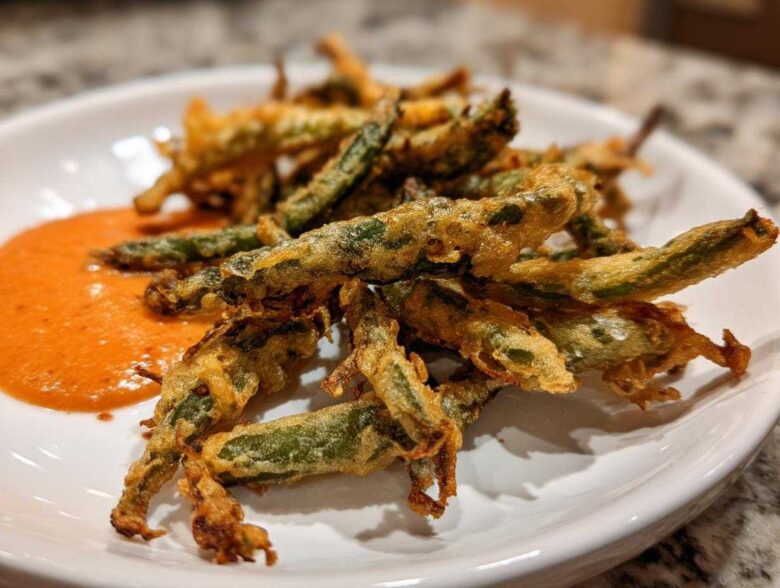 A plate of golden brown Air Fryer Crispy Tempura Green Beans served with a side of orange dipping sauce.