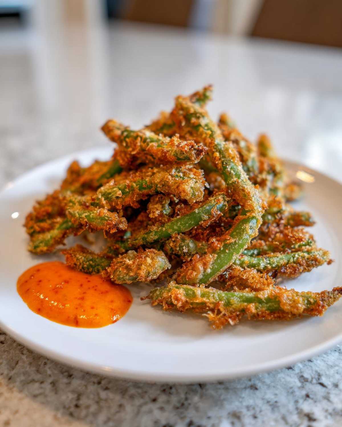 A pile of golden brown Air Fryer Crispy Tempura Green Beans served on a white plate next to a dollop of orange dipping sauce.