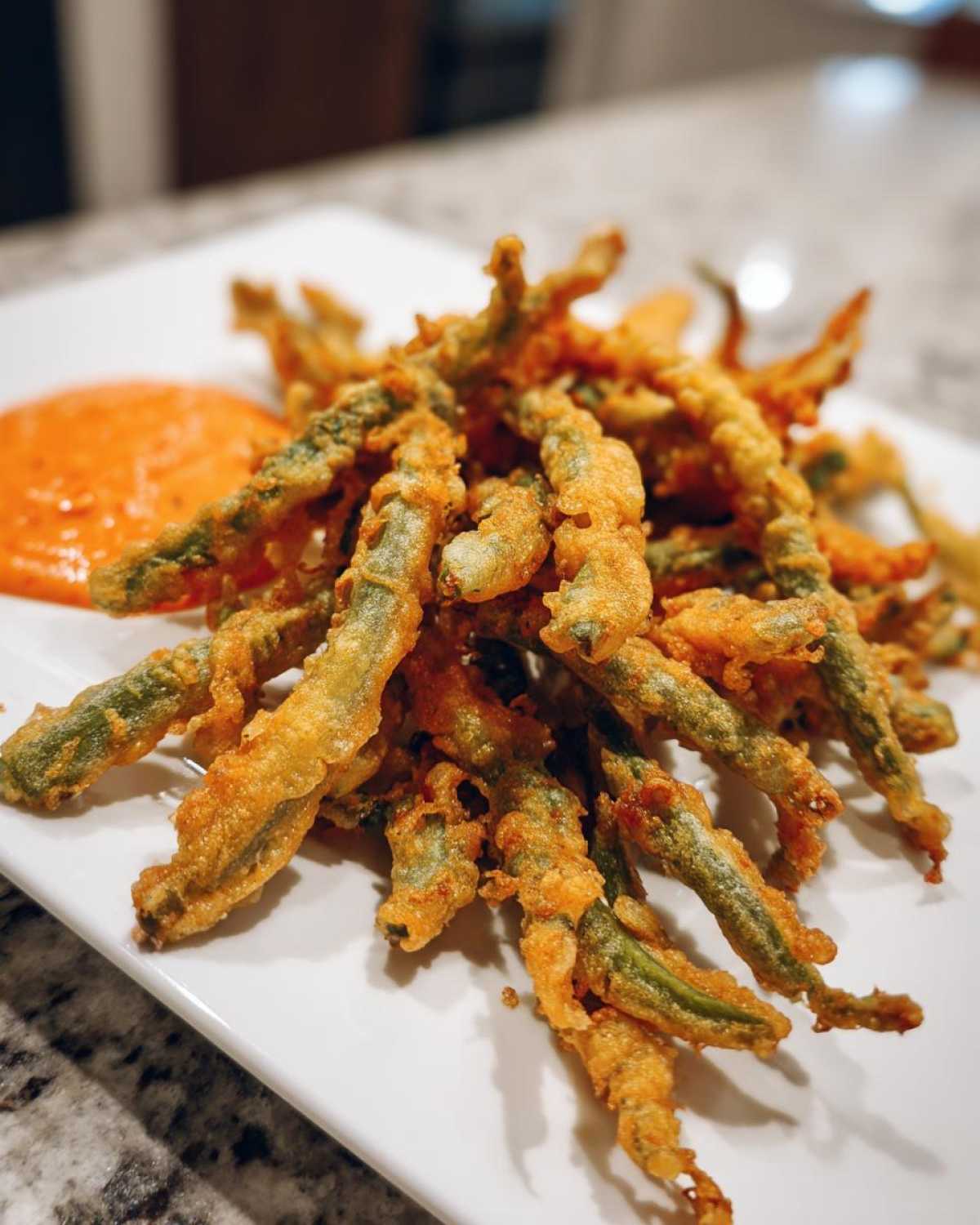 A pile of golden brown Air Fryer Crispy Tempura Green Beans served with a side of orange dipping sauce.