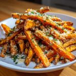 A close-up of crispy Air Fryer Garlic Parmesan Sweet Potato Fries piled high on a white plate, topped with grated cheese and parsley.