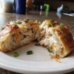 A Copycat Costco Chicken Bake cut in half showing shredded chicken, melted cheese, and green onions inside a golden crust.