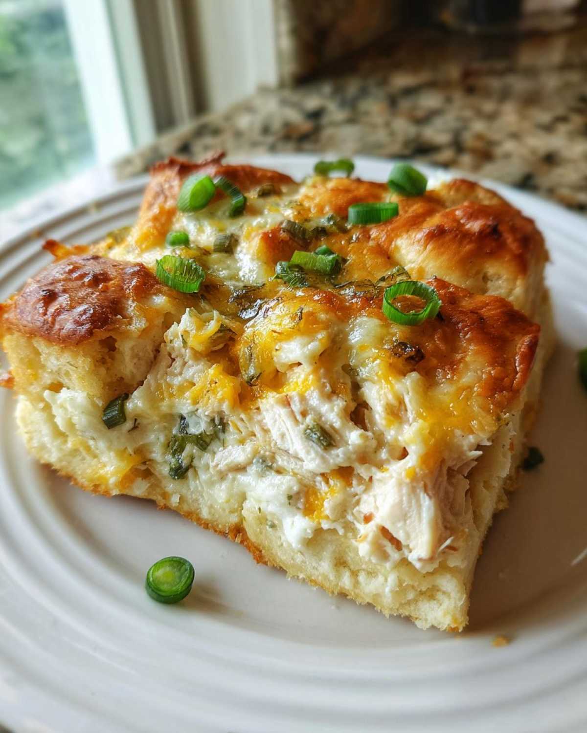 A thick slice of Copycat Costco Chicken Bake showing cheesy chicken filling on a biscuit crust, topped with green onions.