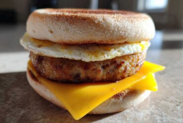 Close-up of a homemade Copycat McDonald's Sausage Egg McMuffin with toasted English muffin, sausage patty, egg, and melted cheese.
