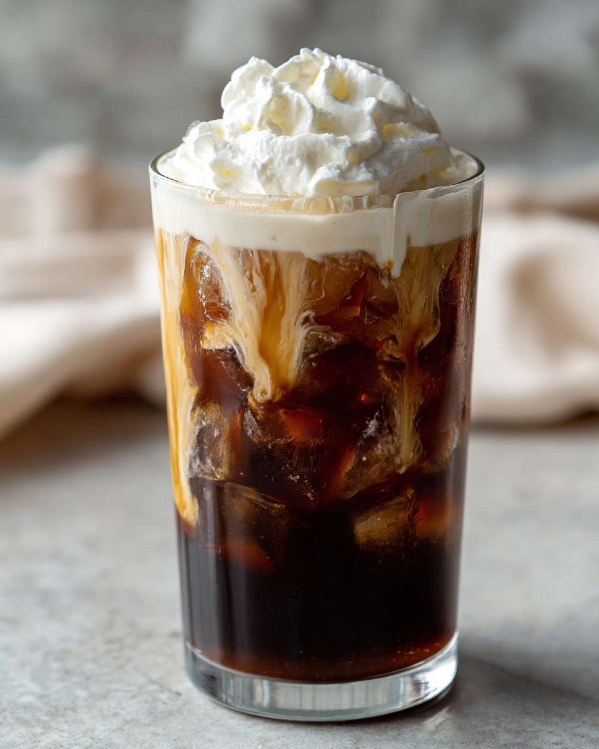 Close-up of a tall glass filled with ice, dark coffee, and swirling white chocolate cream, topped with whipped cream, resembling a Copycat Starbucks Iced White Chocolate Mocha.