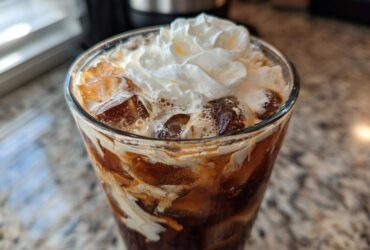 Close-up of a tall glass filled with an iced white chocolate mocha, ice cubes, and topped with whipped cream.