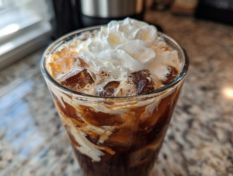 Close-up of a tall glass filled with an iced white chocolate mocha, ice cubes, and topped with whipped cream.