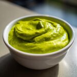 Close-up of vibrant green Creamy Avocado Cilantro Sauce swirled thickly in a small white dipping bowl.