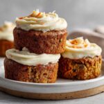 Three Gluten-Free Carrot Cake Cupcakes stacked and arranged on a plate, topped with cream cheese frosting.