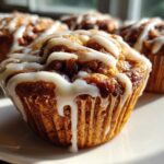 Close-up of a freshly baked Gluten-Free Cinnamon Roll Muffin topped with thick white icing drizzle.