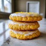 A stack of three bright yellow Gluten-Free Lemon Sugar Cookies topped with white glaze and lemon zest.