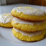 A stack of three bright yellow Gluten-Free Lemon Sugar Cookies topped with white glaze and lemon zest.