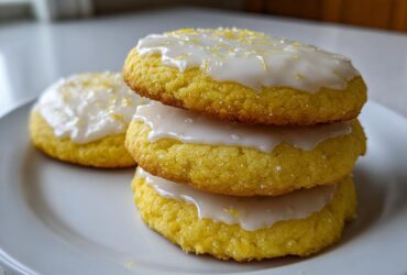 A stack of three bright yellow Gluten-Free Lemon Sugar Cookies topped with white glaze and lemon zest.