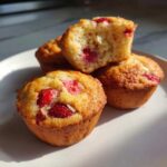 Close-up of golden Gluten-Free Strawberry Almond Muffins, one broken open showing the moist interior and strawberries.