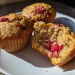 Close-up of three Gluten-Free Strawberry Almond Muffins on a white plate, one broken open showing the moist interior and bright red fruit.