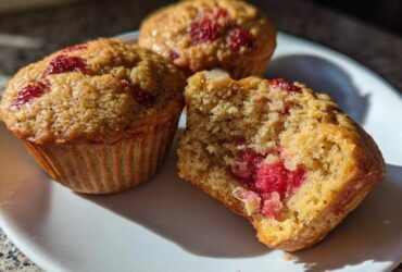 Close-up of three Gluten-Free Strawberry Almond Muffins on a white plate, one broken open showing the moist interior and bright red fruit.