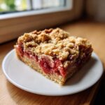 A close-up of a single serving of Gluten-Free Strawberry Rhubarb Bars with a thick crumble topping.