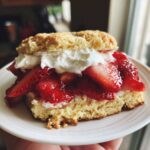 A close-up of a serving of Gluten-Free Strawberry Shortcake Biscuits filled with macerated strawberries and whipped cream.