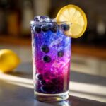 Close-up of Iced Blueberry Lavender Lemonade showing vibrant blue and purple layers, filled with blueberries and ice, garnished with a lemon slice.