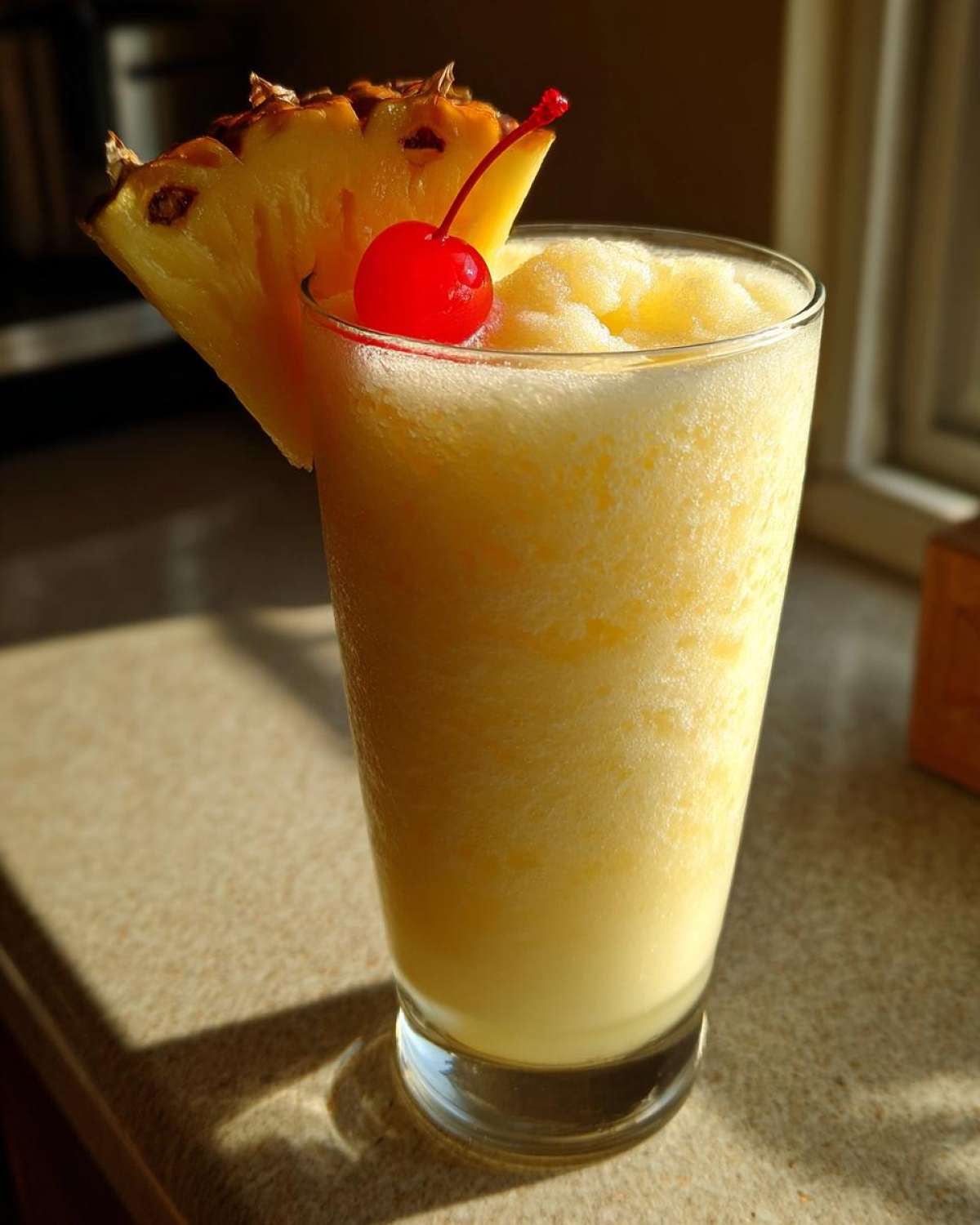 A tall glass filled with a frosty Iced Pineapple Coconut Mocktail, garnished with a pineapple wedge and a maraschino cherry.