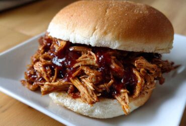 A close-up of a juicy Instant Pot BBQ Pulled Chicken Sandwich piled high on a white plate.