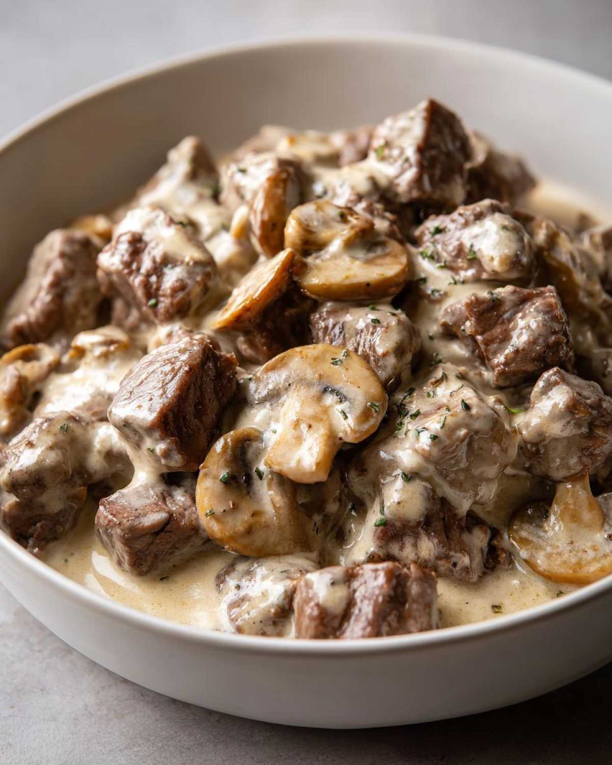 Close-up of tender beef chunks and sliced mushrooms coated in creamy sauce in a white bowl, featuring Instant Pot Beef Stroganoff with Mushrooms.