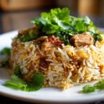 A serving of fluffy Instant Pot Chicken Biryani mounded on a white plate and topped with fresh cilantro.