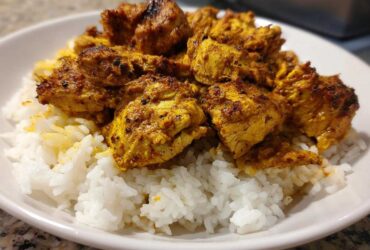 Close-up of seasoned, golden-brown chicken shawarma pieces served over fluffy white rice in a white bowl.