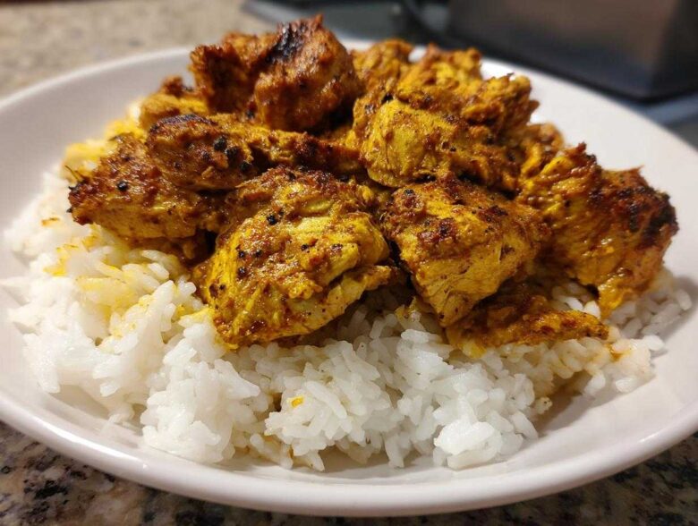 Close-up of seasoned, golden-brown chicken shawarma pieces served over fluffy white rice in a white bowl.