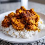 Close-up of seasoned, orange-hued Instant Pot Chicken Shawarma Rice served over fluffy white rice on a white plate.
