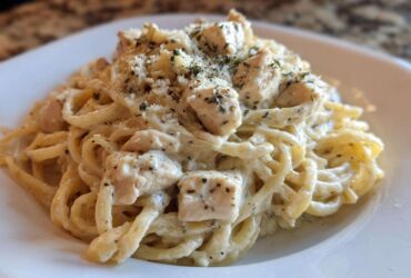 A close-up of Instant Pot Creamy Chicken Alfredo Pasta served on a white plate, topped with Parmesan and herbs.