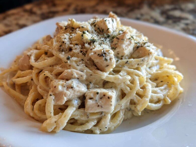 A close-up of Instant Pot Creamy Chicken Alfredo Pasta served on a white plate, topped with Parmesan and herbs.
