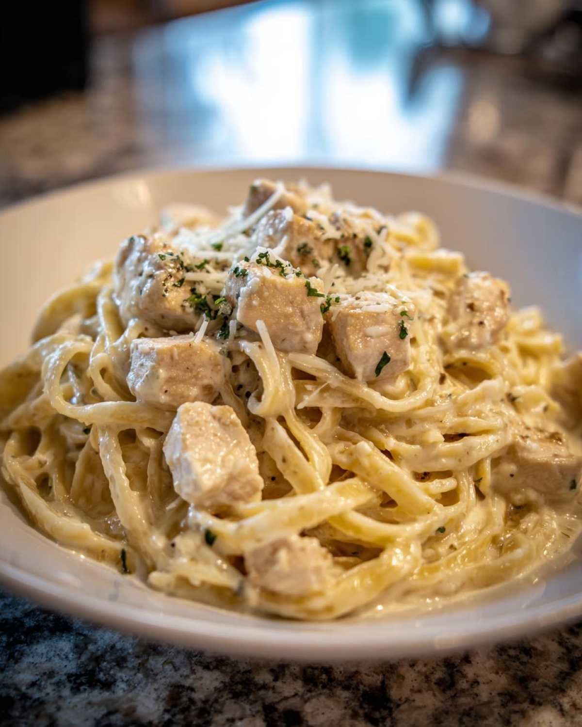 A close-up shot of a white bowl filled with Instant Pot Creamy Chicken Alfredo Pasta, topped with cubed chicken and grated cheese.