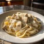 A close-up of a white bowl filled with Instant Pot Creamy Chicken Alfredo Pasta, topped with diced chicken and grated Parmesan.