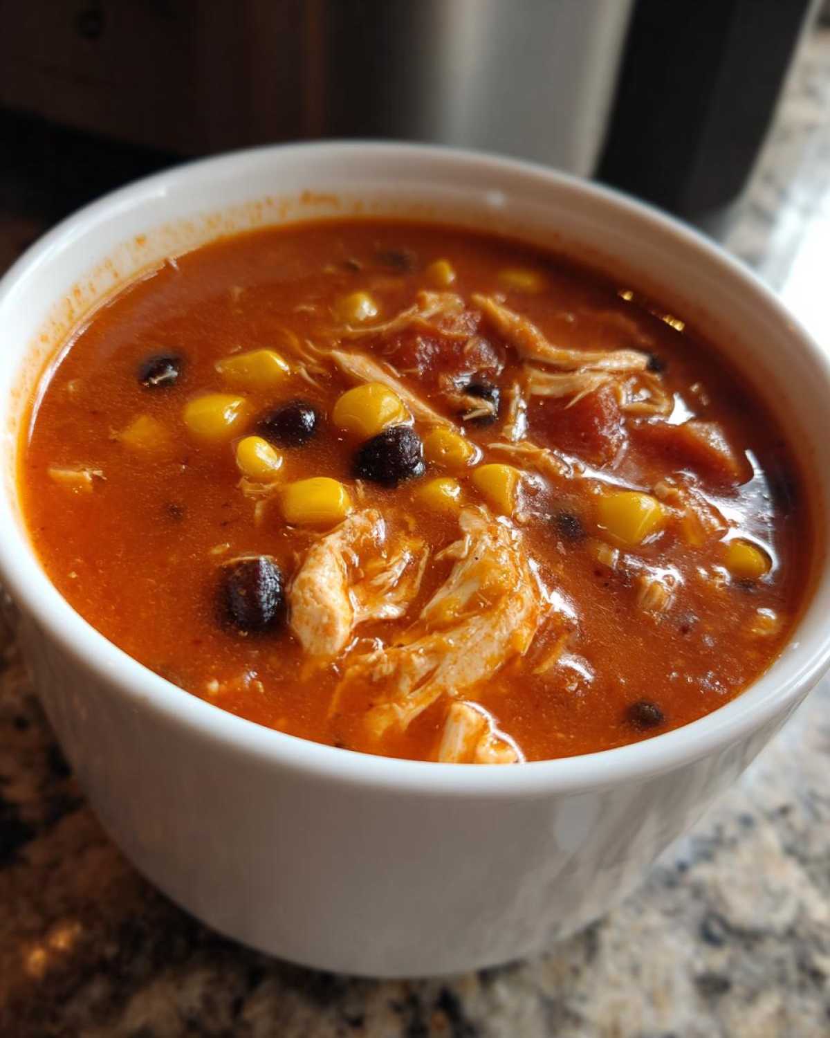 Close-up of a white bowl filled with rich, red Instant Pot Creamy Chicken Taco Soup containing shredded chicken, corn, and black beans.