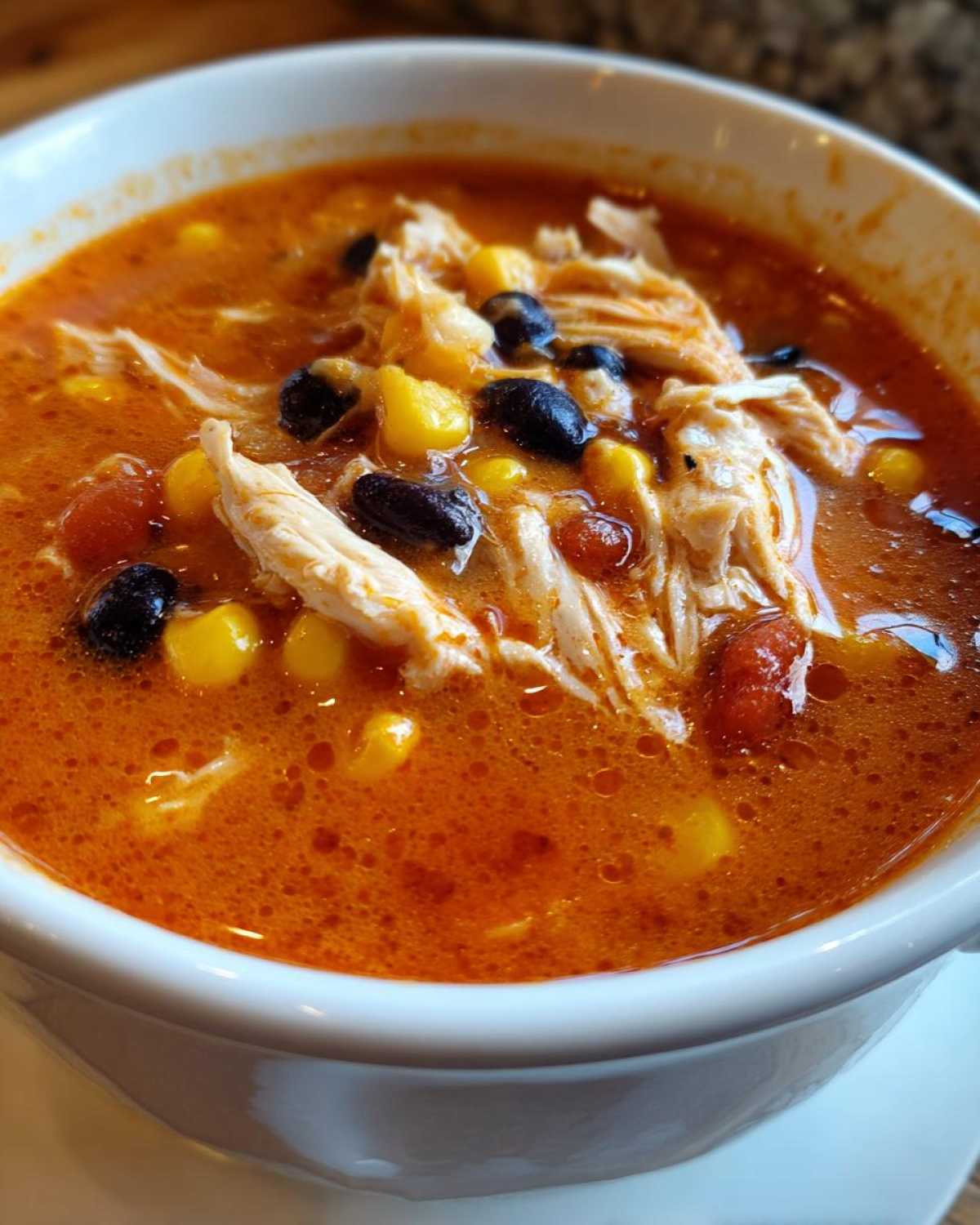 A close-up view of a white bowl filled with Instant Pot Creamy Chicken Taco Soup, showing shredded chicken, black beans, and corn in a rich orange broth.