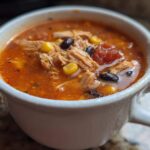 Close-up of a white mug filled with steaming Instant Pot Creamy Chicken Taco Soup, showing shredded chicken, corn, and black beans.