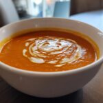 A close-up of a white bowl filled with vibrant orange Instant Pot Creamy Tomato Bisque, swirled with cream on top.