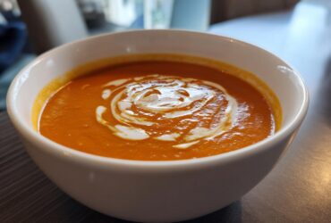 A close-up of a white bowl filled with vibrant orange Instant Pot Creamy Tomato Bisque, swirled with cream on top.