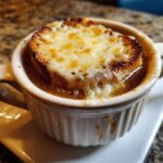 Close-up of Instant Pot French Onion Soup topped with melted, bubbly Gruyère cheese over a crouton.
