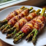 Four bundles of perfectly cooked Keto Bacon Wrapped Asparagus Bundles topped with melted cheese, served on a white plate.