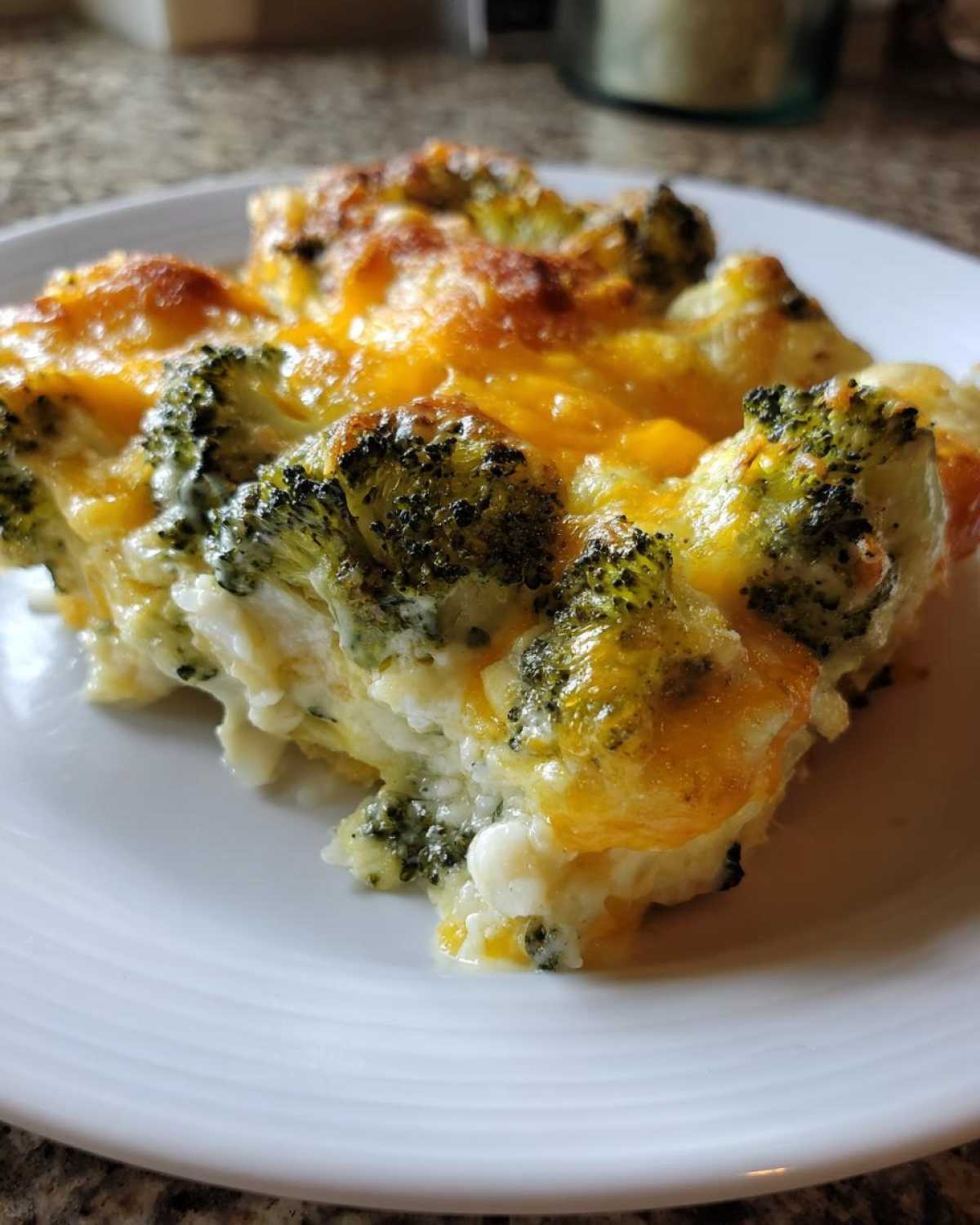 A close-up serving of Keto Cheesy Broccoli Casserole topped with melted, browned cheddar cheese.