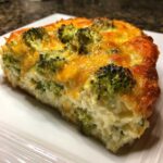 Close-up of a thick slice of Keto Cheesy Broccoli Casserole with a creamy base and melted cheddar cheese topping.
