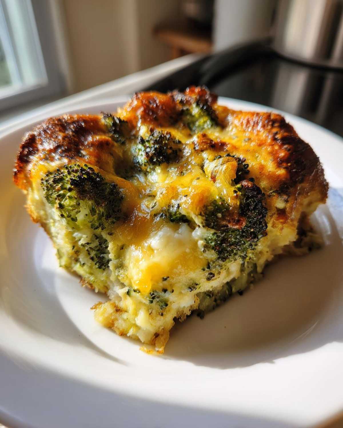 A close-up shot of a golden-brown slice of Keto Cheesy Broccoli Casserole on a white plate.