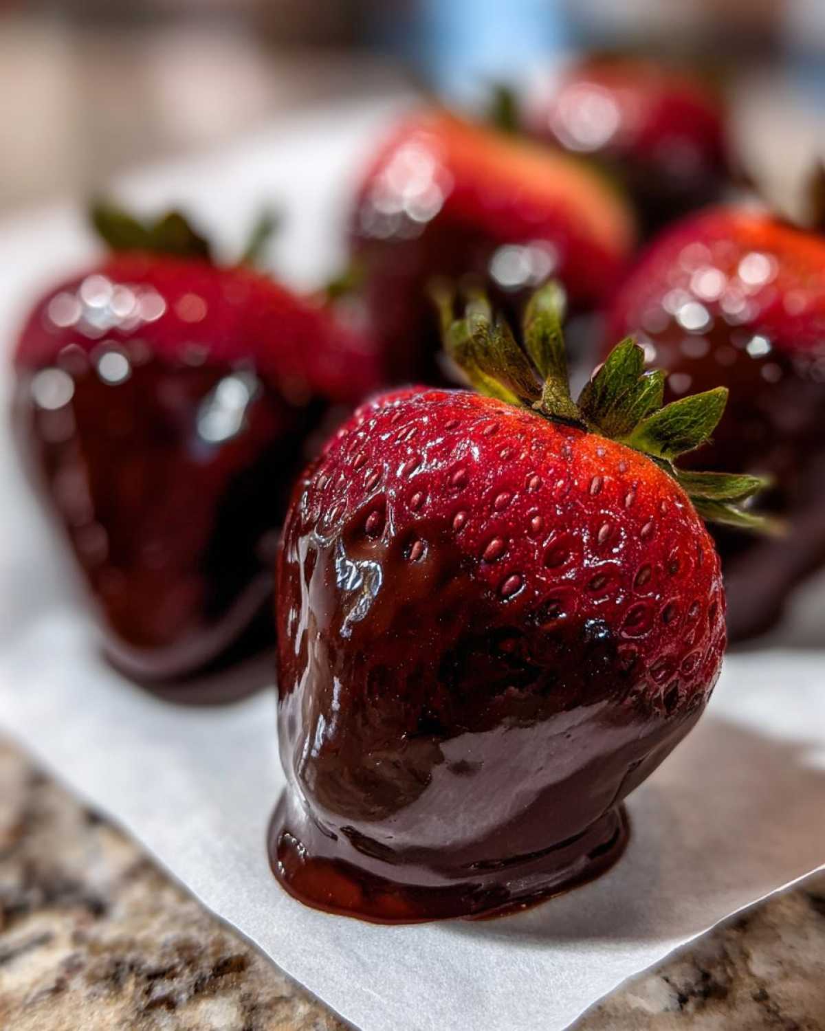 A close-up of a freshly dipped Keto Chocolate Covered Strawberry resting on parchment paper.