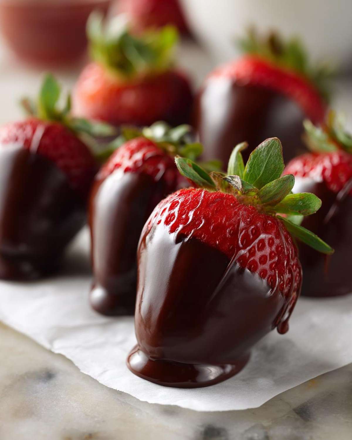 A close-up of freshly dipped Keto Chocolate Covered Strawberries resting on parchment paper.