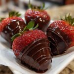 Four fresh strawberries partially dipped in dark chocolate, featuring a decorative chocolate drizzle, perfect for Keto Chocolate Covered Strawberries.
