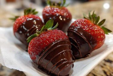 Four fresh strawberries partially dipped in dark chocolate, featuring a decorative chocolate drizzle, perfect for Keto Chocolate Covered Strawberries.