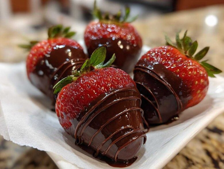 Four fresh strawberries partially dipped in dark chocolate, featuring a decorative chocolate drizzle, perfect for Keto Chocolate Covered Strawberries.