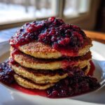 A stack of fluffy Keto Coconut Flour Pancakes topped generously with homemade berry sauce.