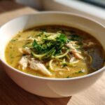A close-up of a white bowl filled with Keto Creamy Chicken Zoodle Soup, featuring shredded chicken and zucchini noodles.